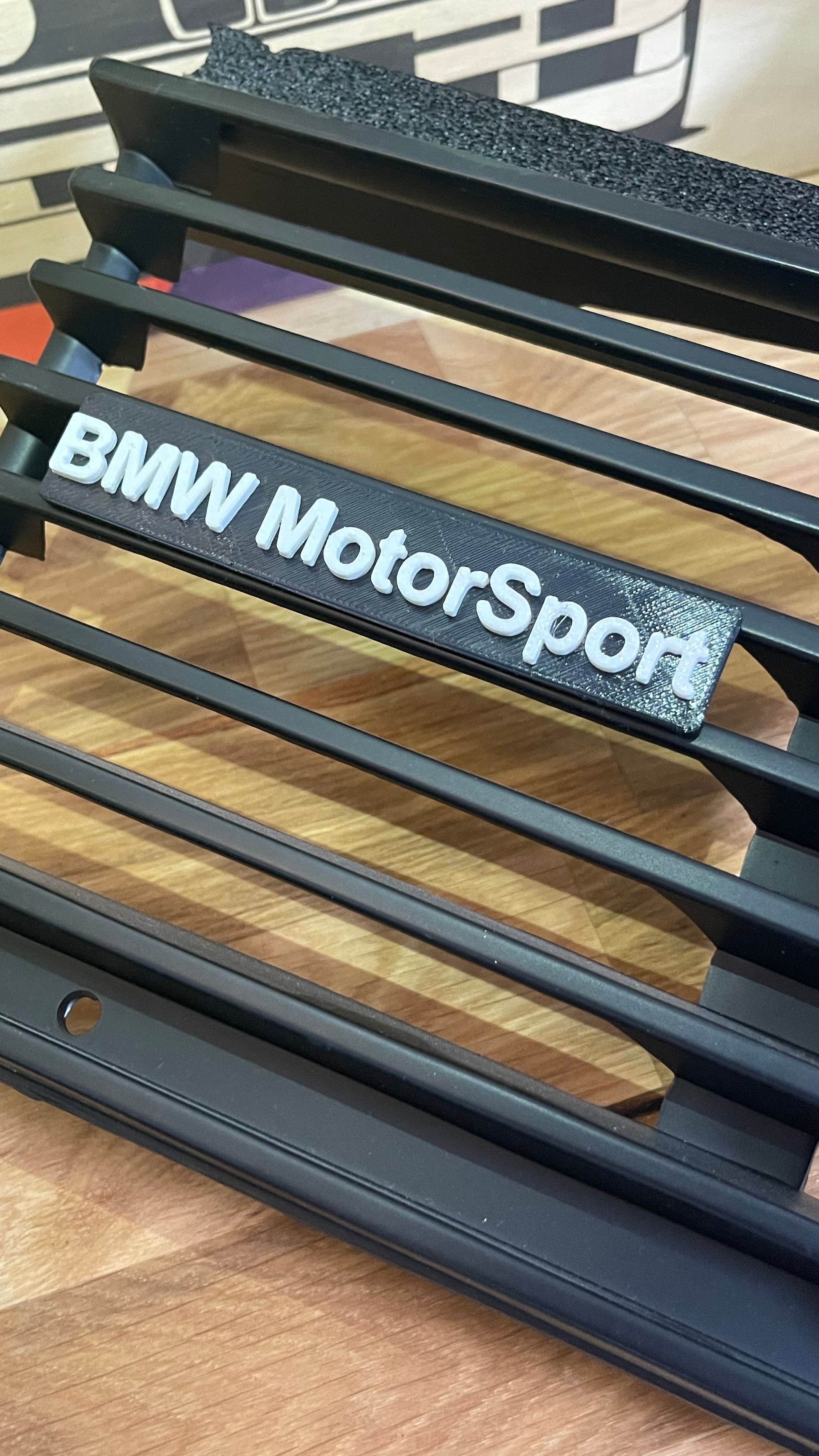 "BMW Motorsport" emblem displayed on a black car grille. 
