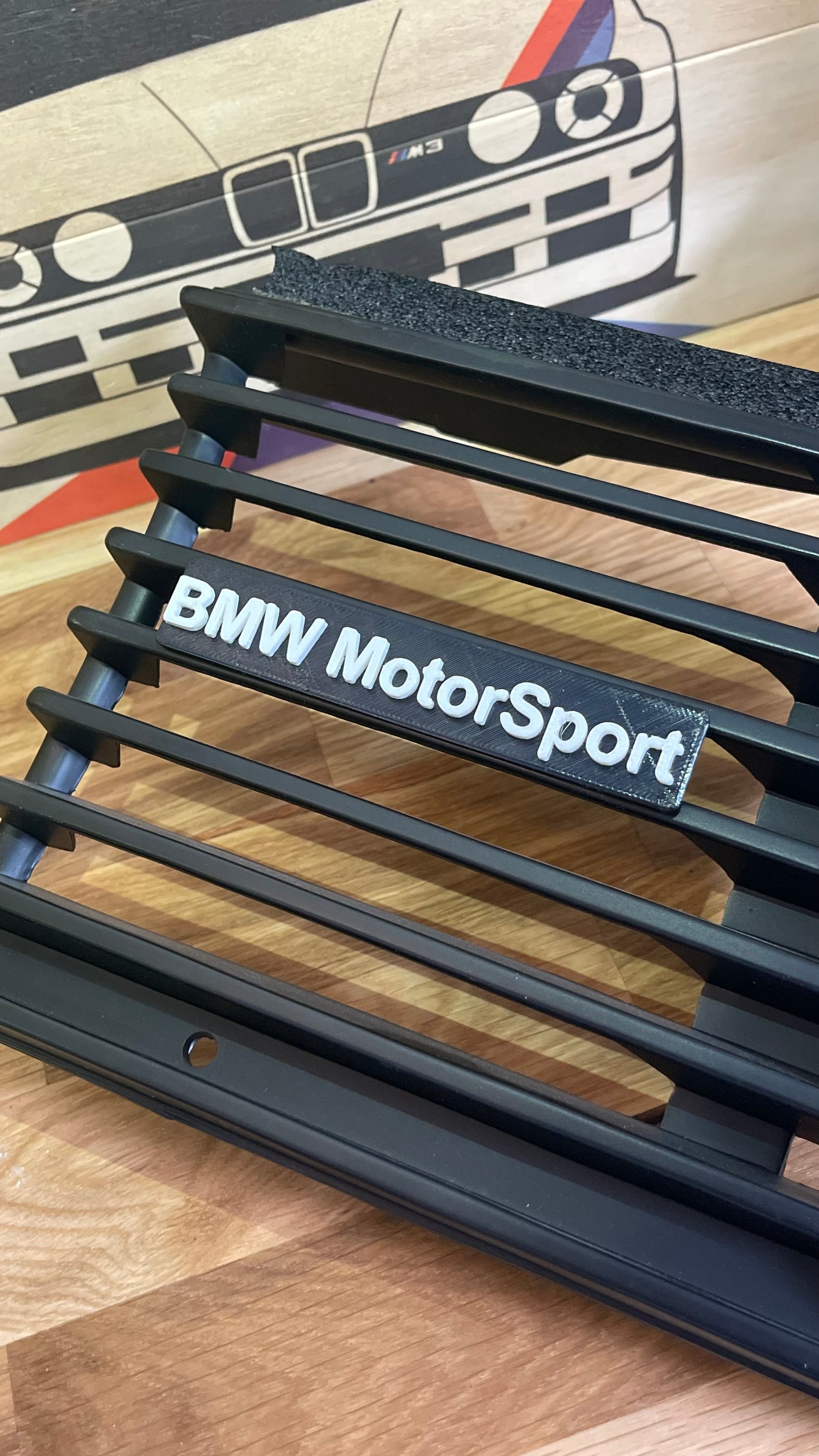 Black BMW kidney grille displays a raised "BMW MotorSport" badge in white lettering. 
