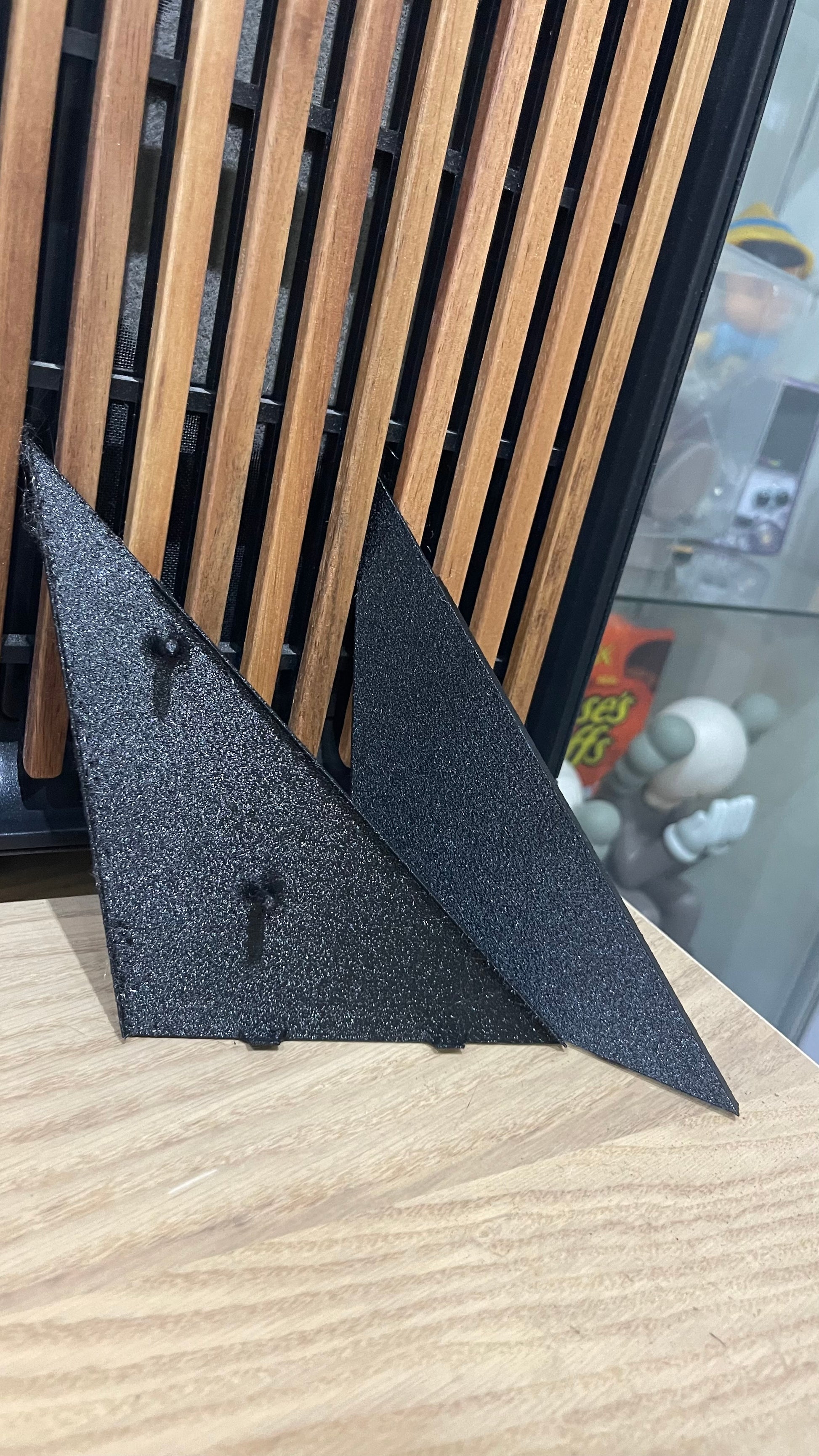 Two black textured triangular supports lean against a wooden slatted surface. 
