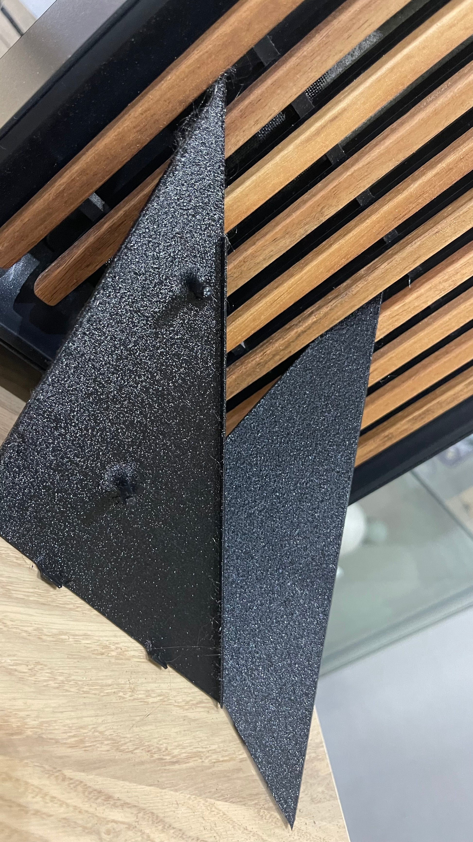 Two black metal brackets support a wooden slatted surface. 
